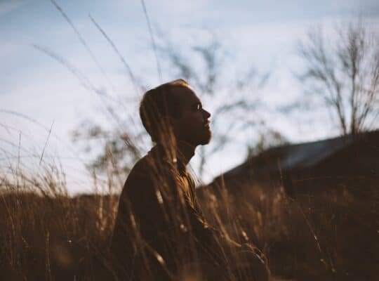 silhouette of man sitting on grass field at daytime